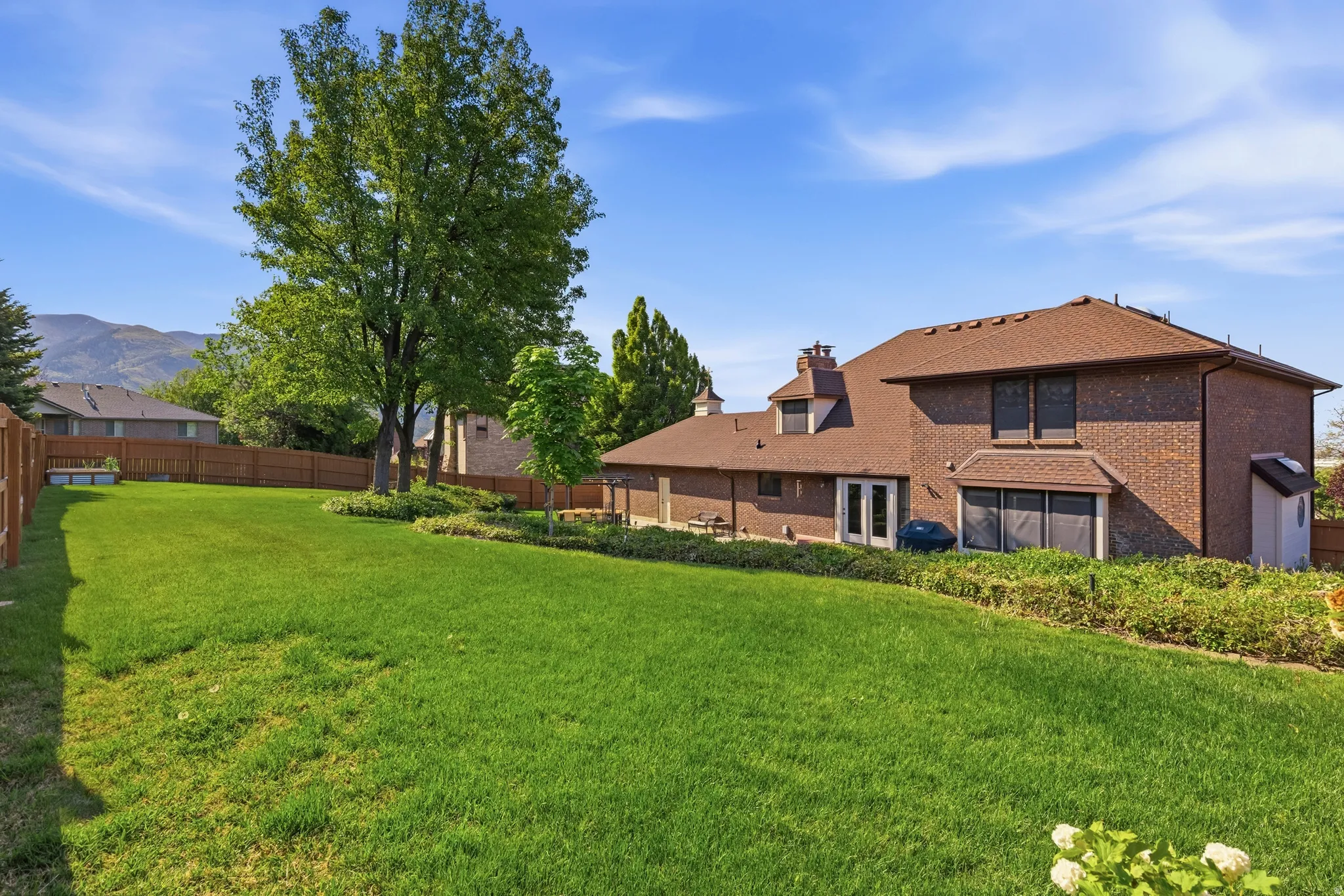 Expansive backyard featuring a manicured lawn, mature trees, and a wooden privacy fence
