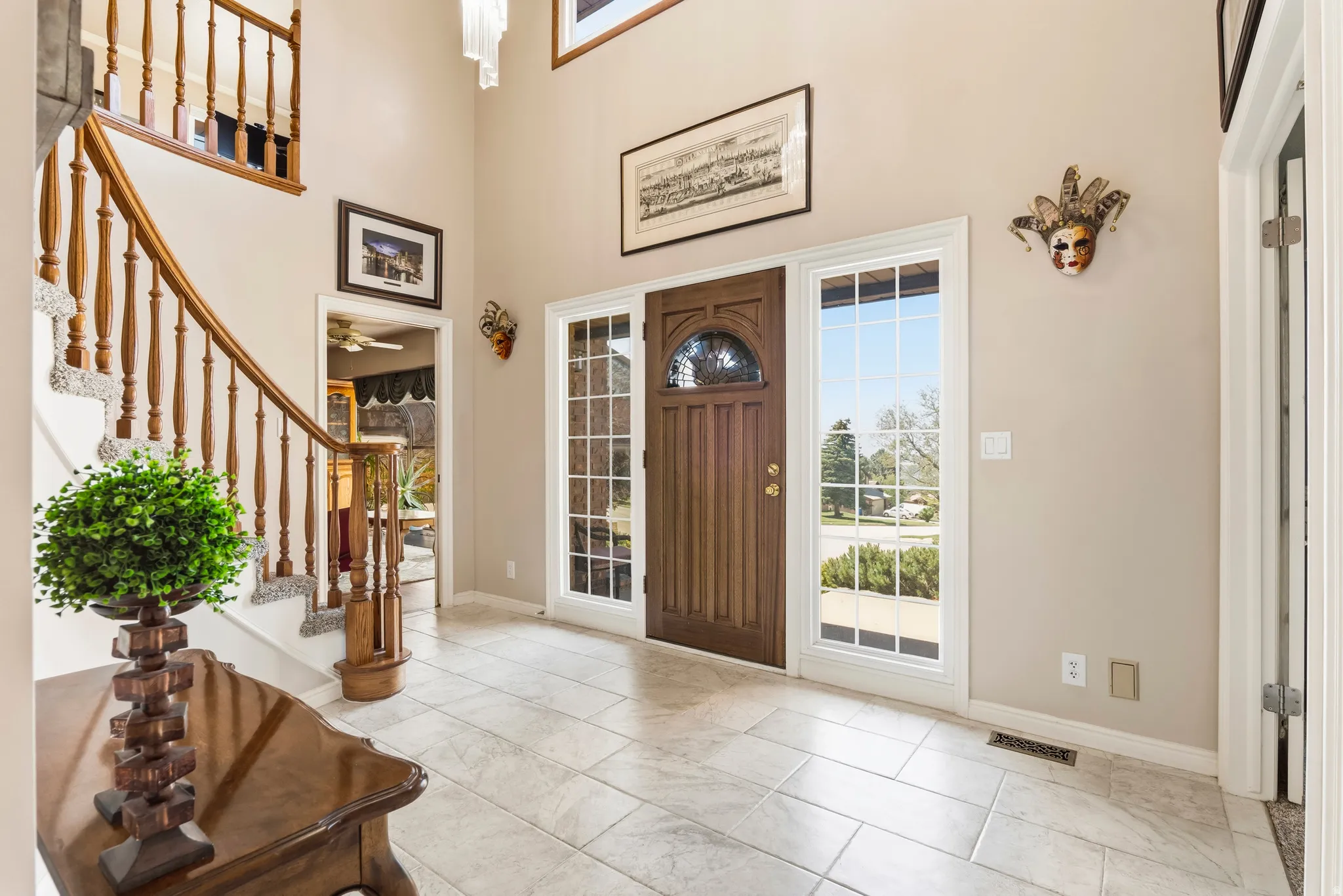Entryway featuring a grand staircase with wood banister, tile flooring, a dark wood front door with an arched window, and two sidelight windows