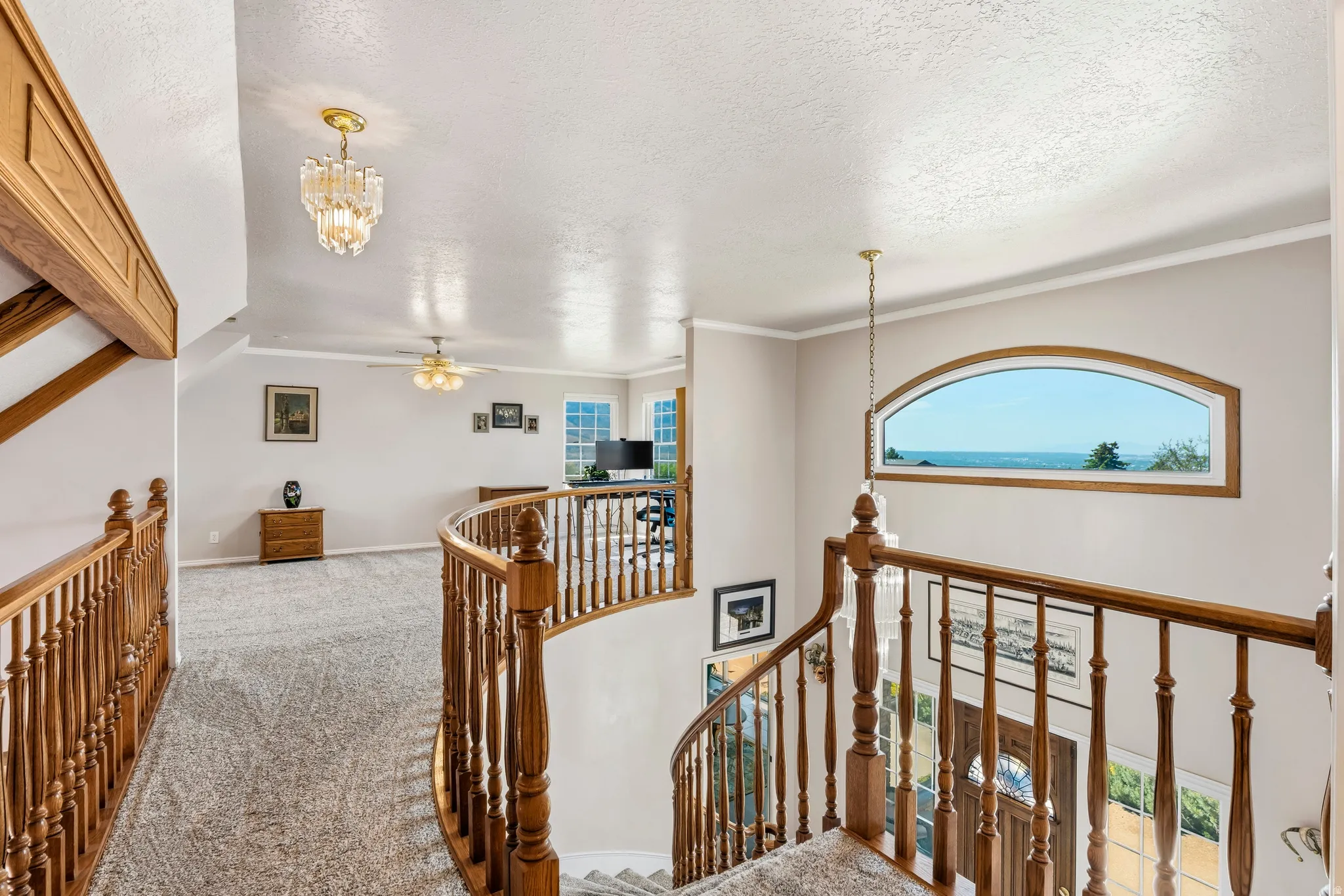 Upper-level landing featuring a curved wood staircase with spindle balusters, a large arch-top window, and light gray wall paint