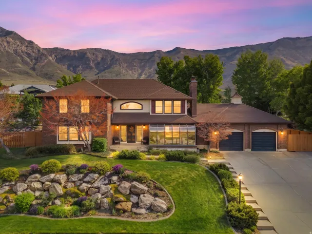 Brick exterior residence featuring a sunroom, a two-car garage with arched entrances, and a stone retaining wall with plantings