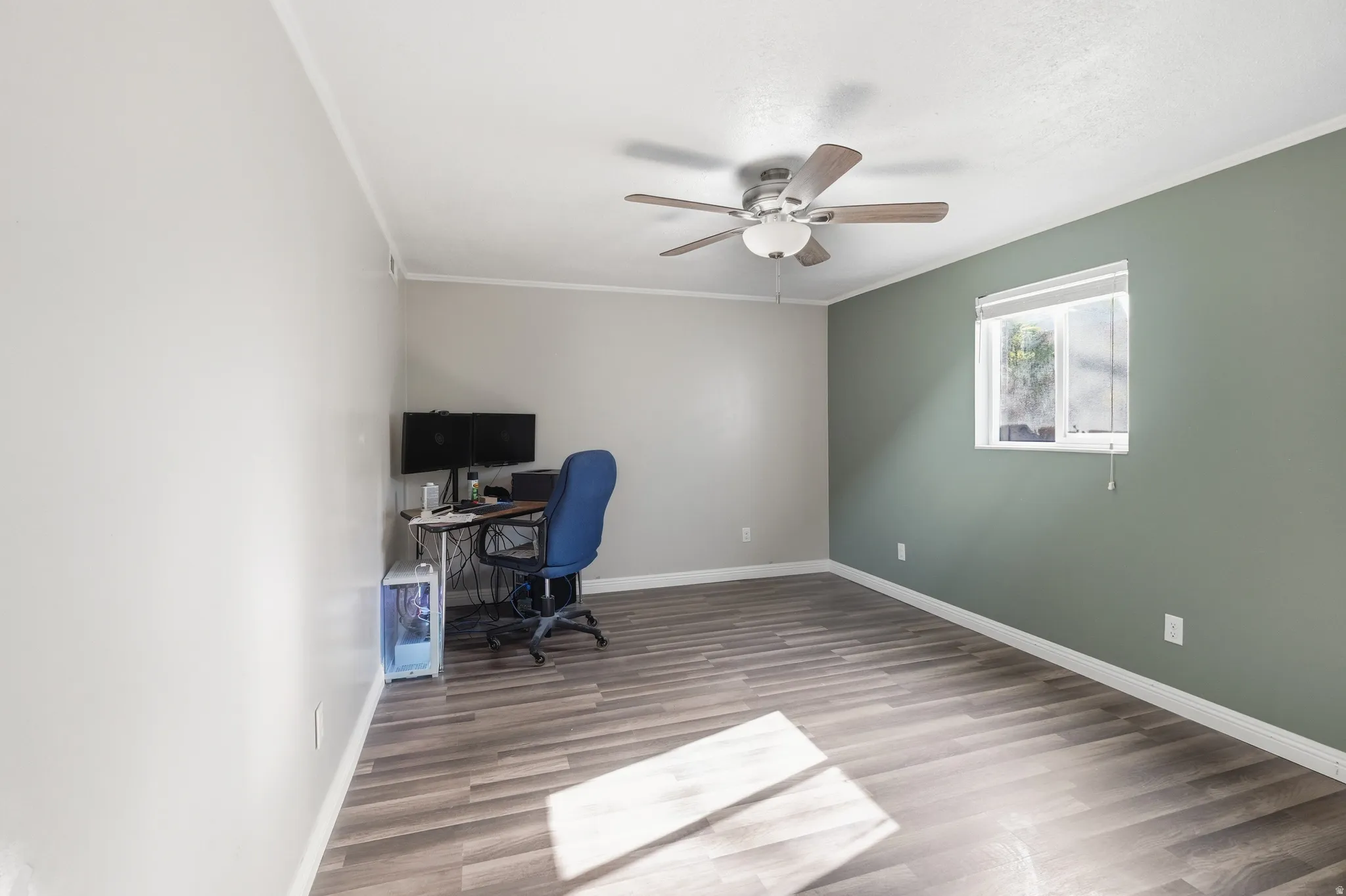 Spacious room featuring wood-finish flooring, a ceiling fan, and a window with blinds