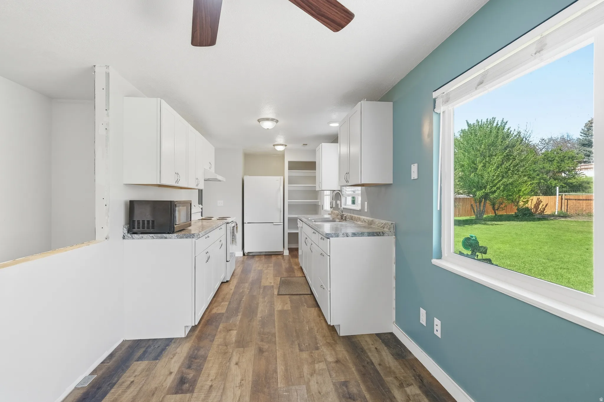 Kitchen featuring wood-finish flooring, white cabinetry, integrated sink, and an expansive window overlooking a green yard