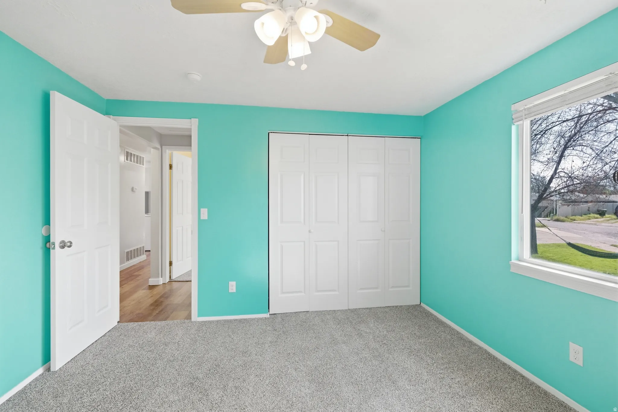 Interior room featuring light teal walls, a neutral carpeted floor, and a white ceiling with a ceiling fan