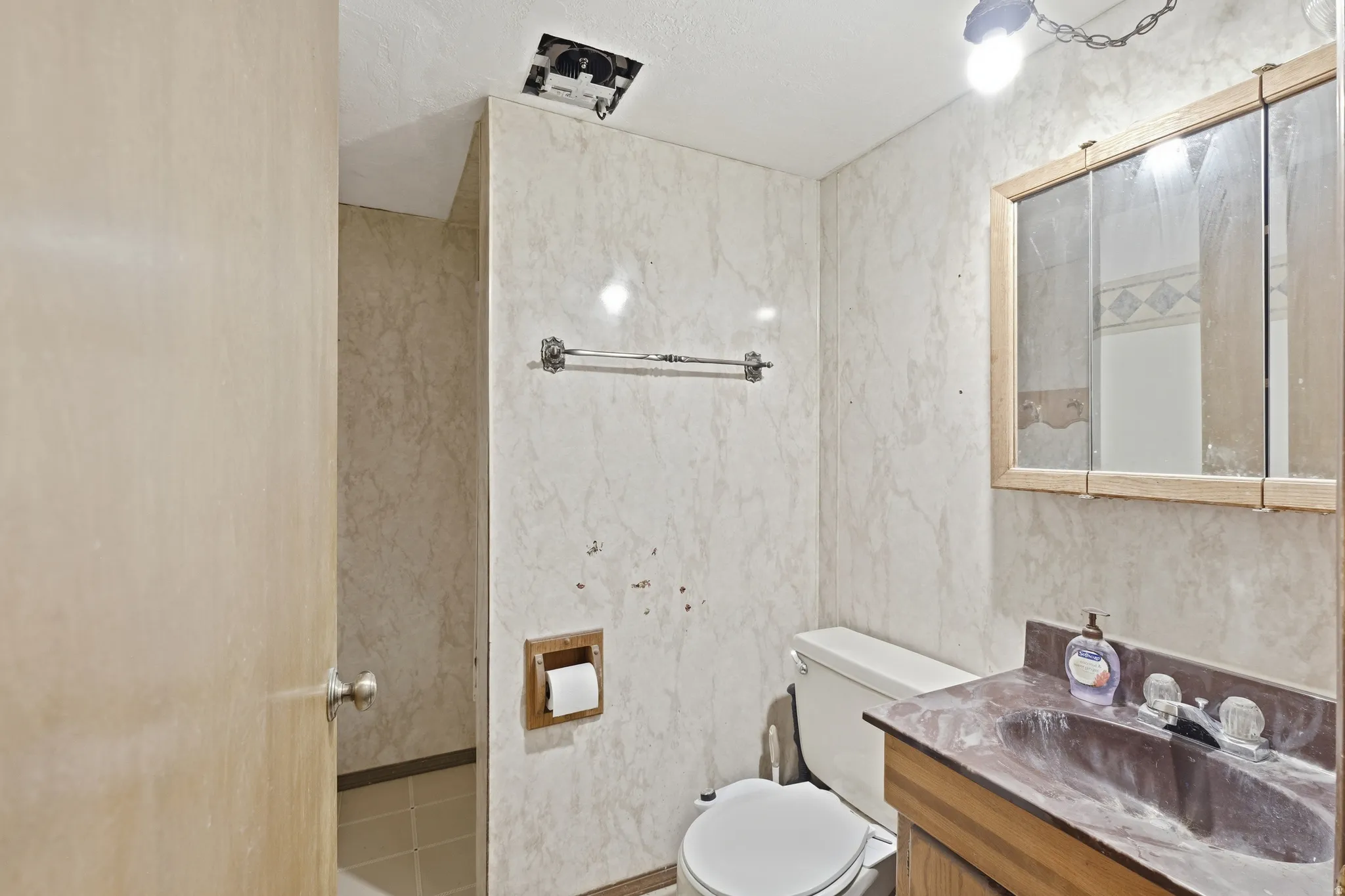 Bathroom featuring a vanity with an integrated sink, a wall-mounted medicine cabinet with a wood-finish frame, and light-toned wall paneling