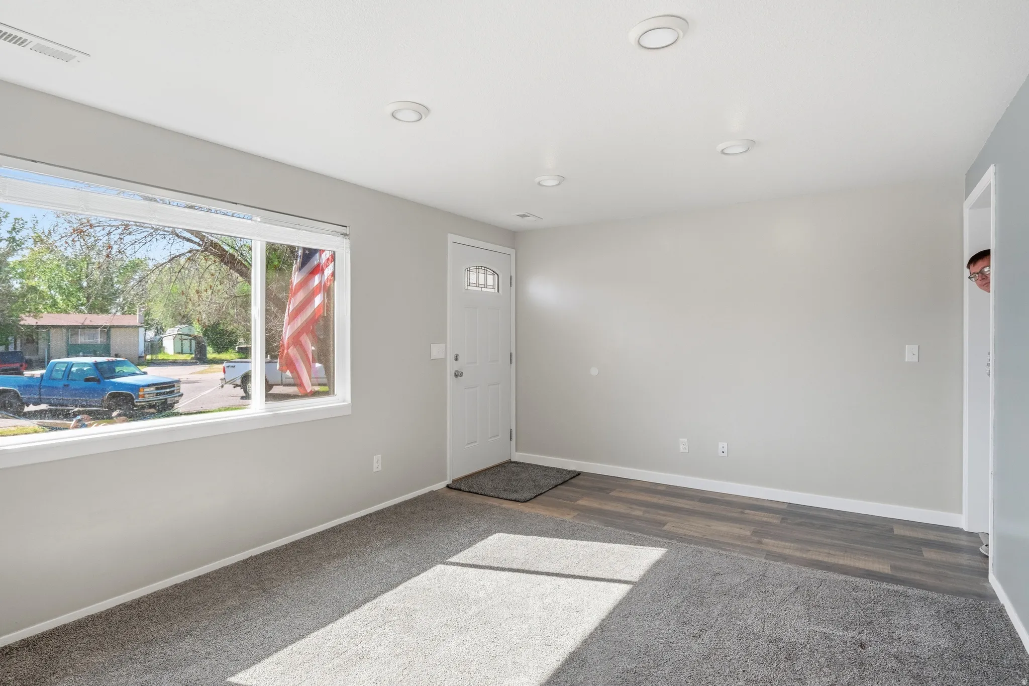 Bright interior space featuring a large picture window, recessed lighting, and a front entry door with decorative glass