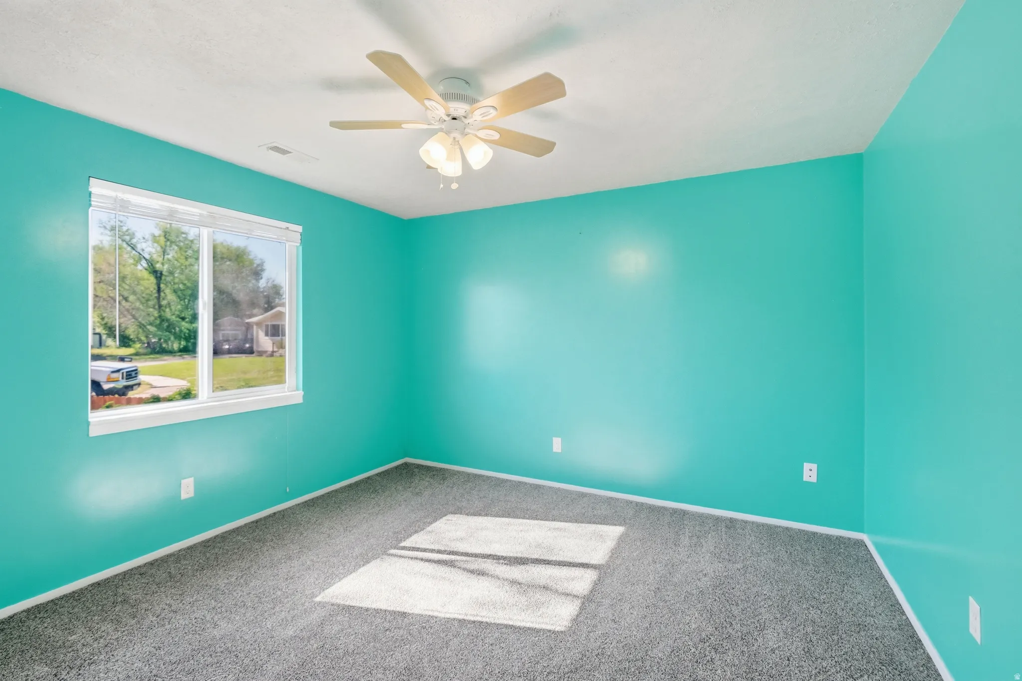 Carpeted room with a ceiling fan light fixture and a large window