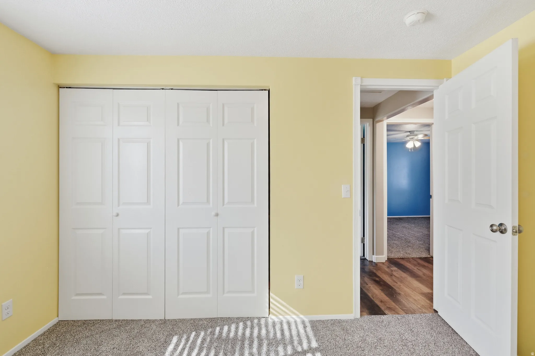 Bedroom featuring light yellow walls, white bi-fold closet doors, and textured gray carpeting