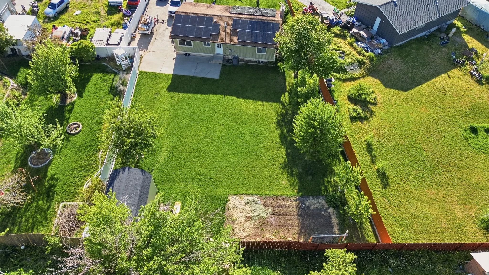 Expansive green lot featuring a residential structure with solar panels, a paved driveway, and established fencing