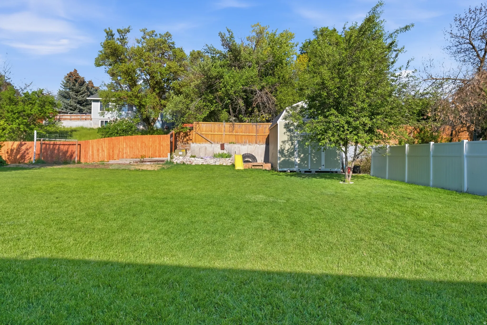 Expansive green lawn with a white privacy fence and wood fencing