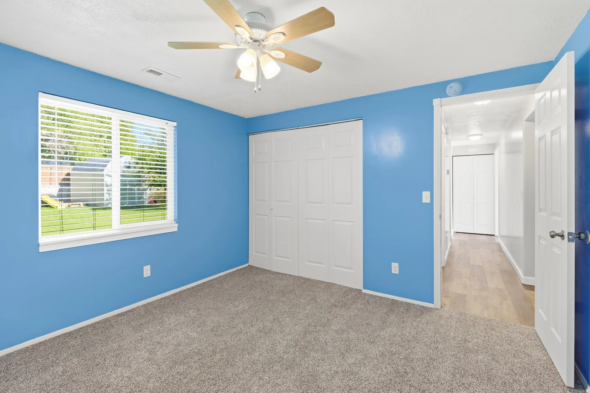 Interior room featuring blue wall finish, gray carpet, a ceiling fan with light, and bi-fold closet doors