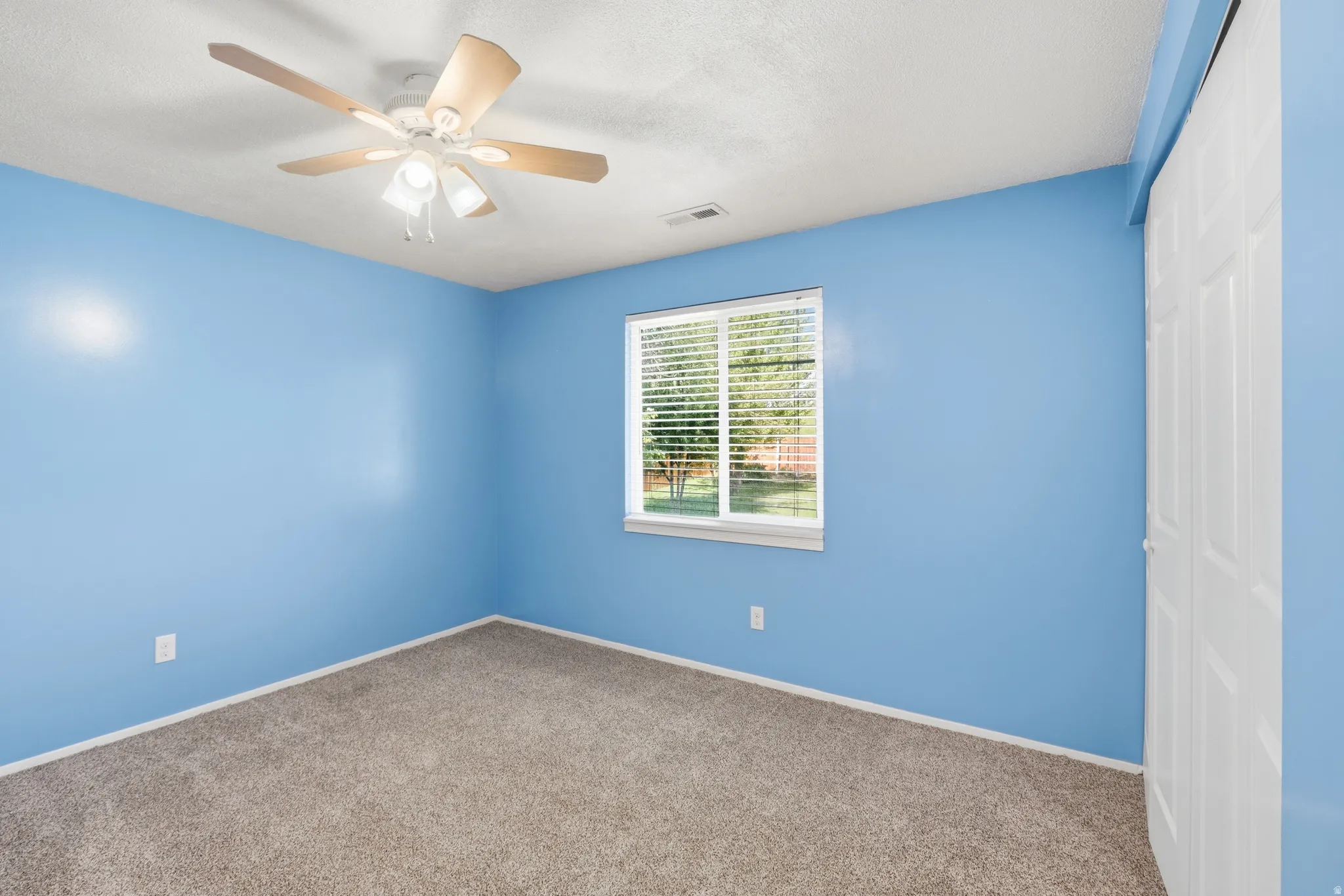 Bedroom featuring a ceiling fan with integrated lighting, a window with horizontal blinds, neutral-toned carpet, and a white bi-fold closet door