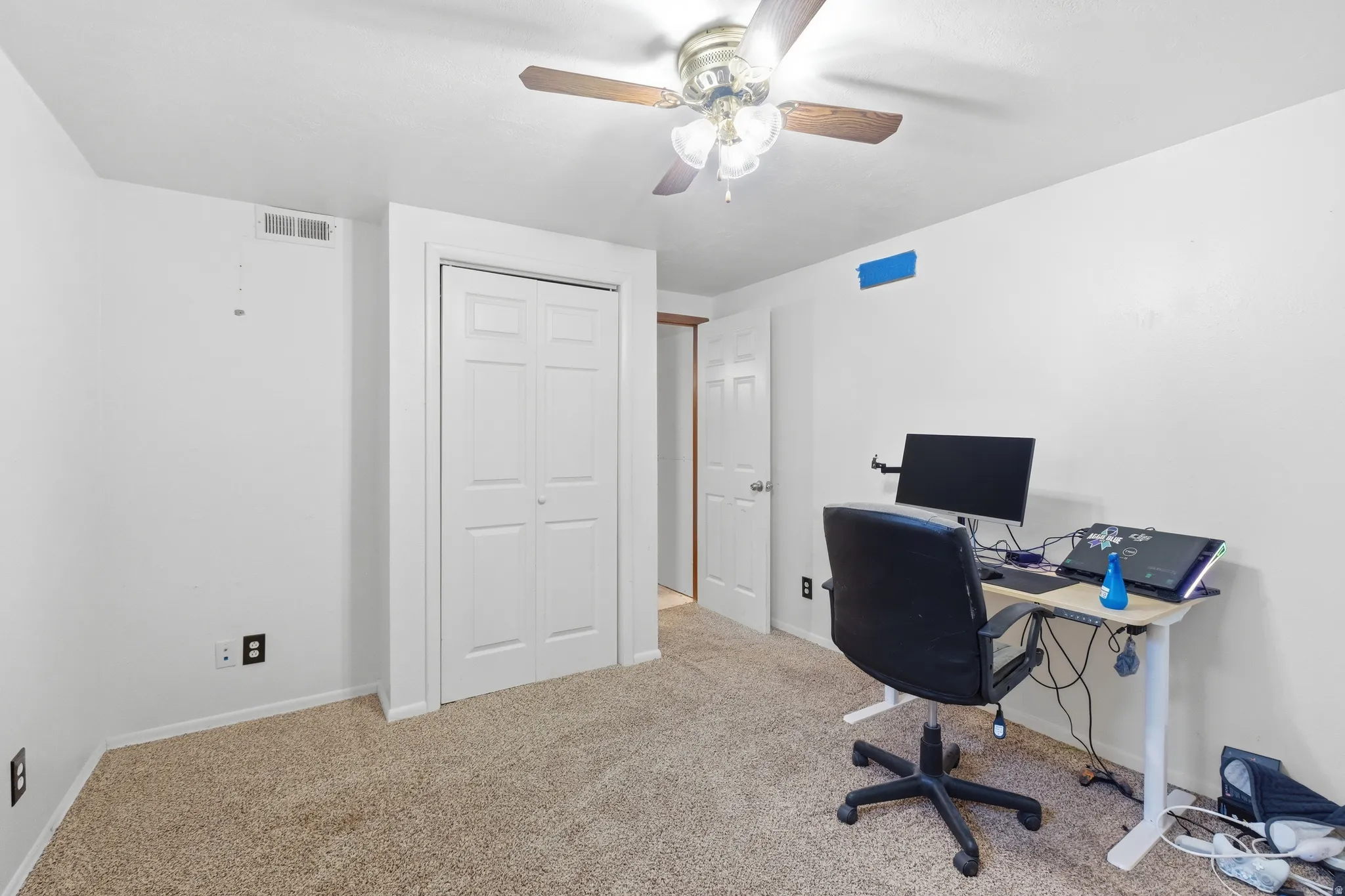 Carpeted room featuring a ceiling fan with light fixture, white bi-fold closet doors, and white painted walls
