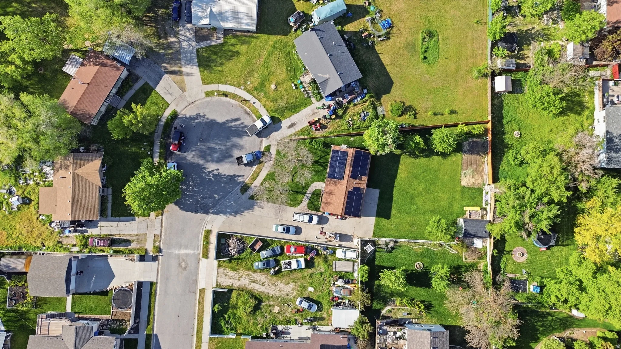 Property with solar panel array on the roof, surrounded by mature trees and a green lawn