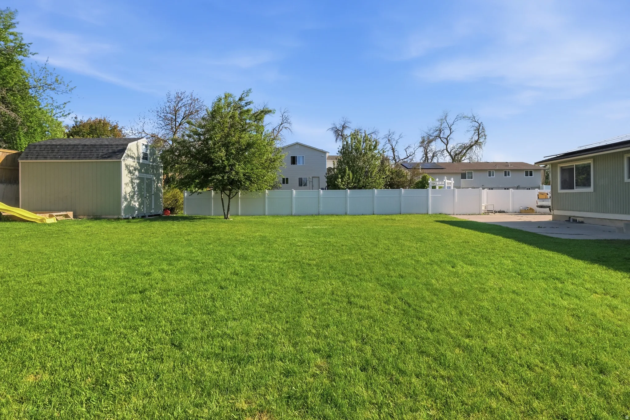 Expansive backyard featuring a large green lawn, full privacy fencing, and a built-in storage shed with a dark shingle roof
