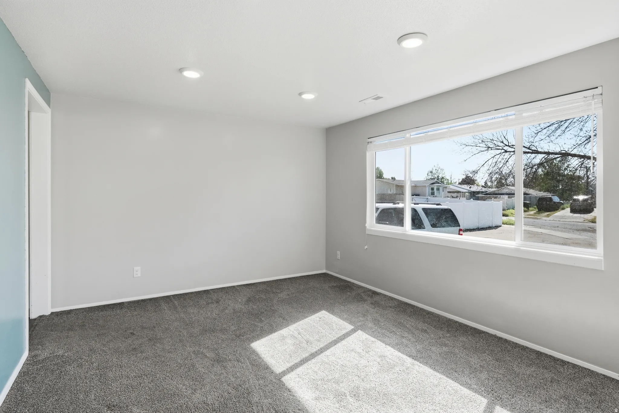 Recessed ceiling lighting, light gray wall paint, contrasting accent wall, gray carpet flooring, and a large window with white blinds