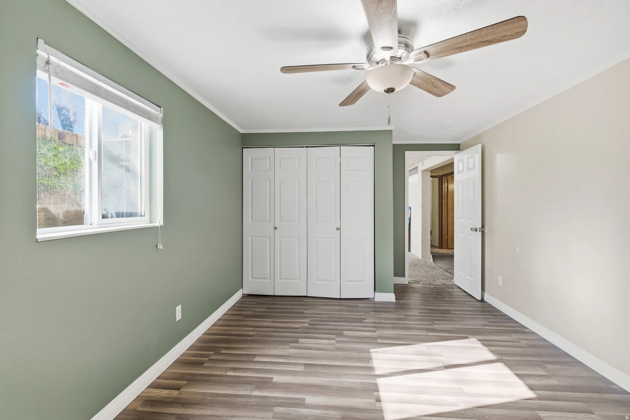 Spacious room featuring wood-finish flooring, a contemporary ceiling fan, and a large window with privacy blinds