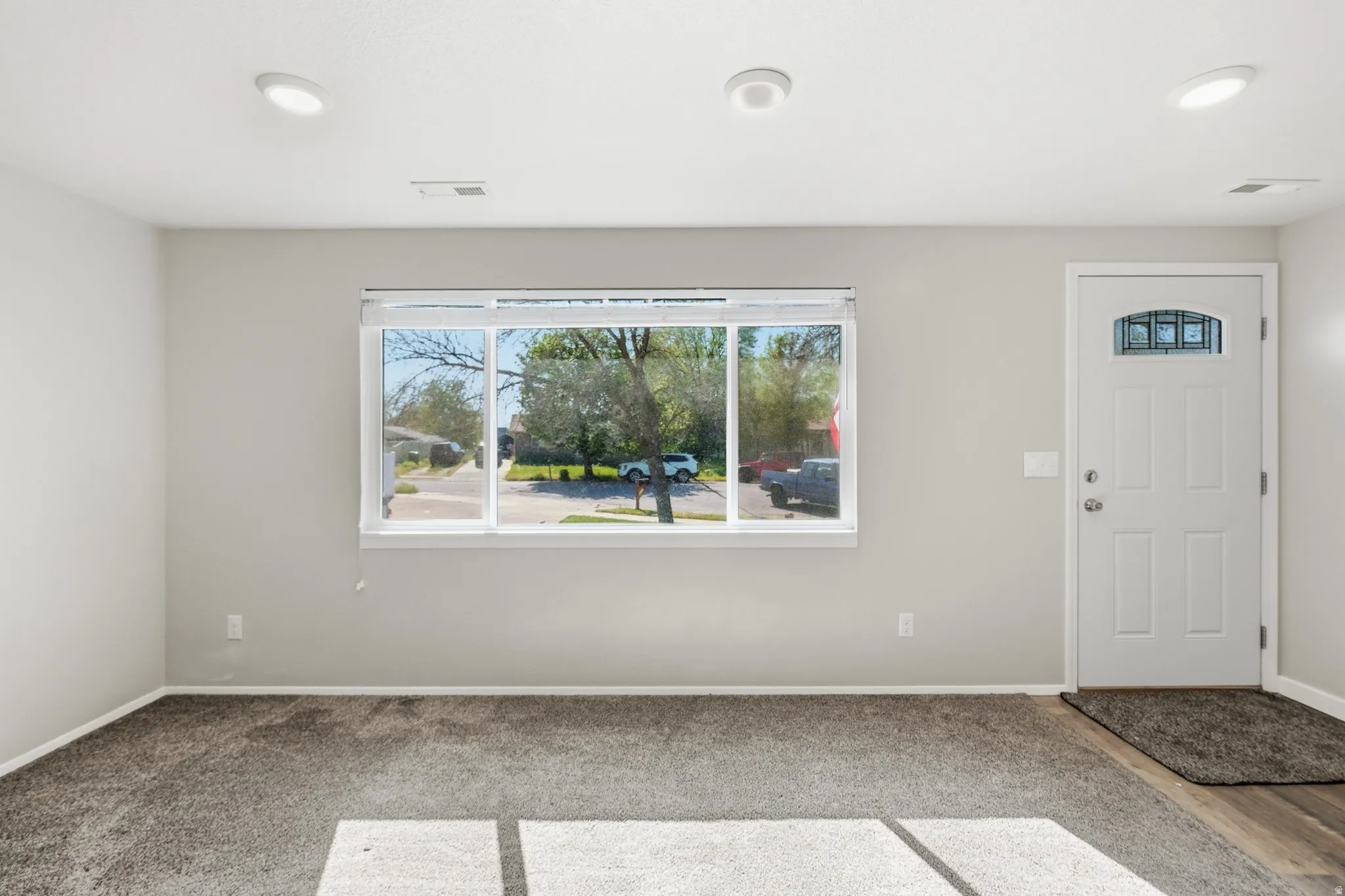 Spacious entry area with light gray walls, dark gray carpeting, and a contrasting wood-finish flooring at the entryway