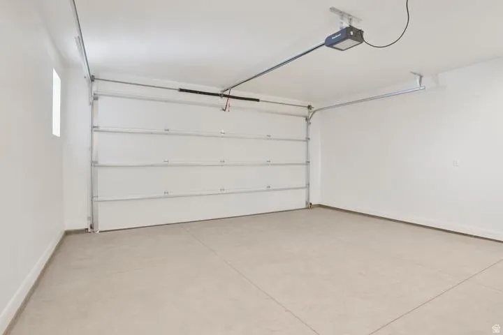 Spacious garage featuring a sectional overhead door, automatic opener, concrete flooring, and a high ceiling