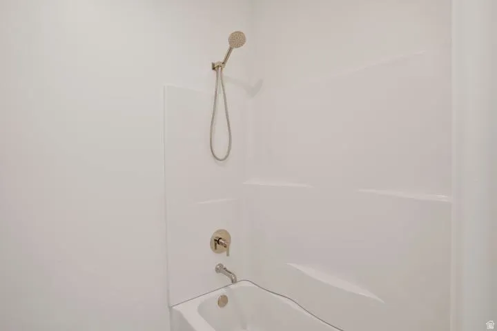 Bathtub and shower combination featuring white surround, brushed nickel fixtures, and a handheld showerhead