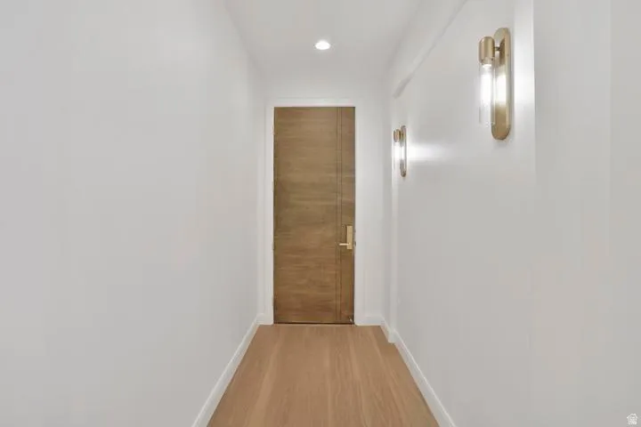 Hallway featuring wood-finish flooring, recessed lighting, and modern brass wall sconces