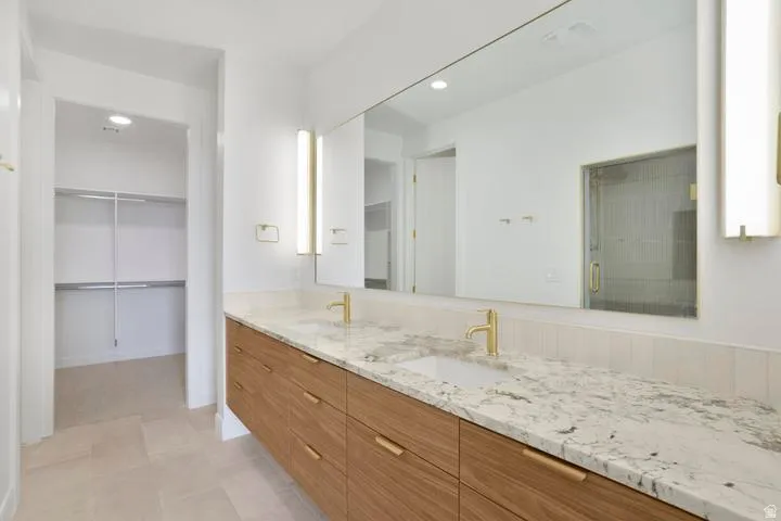 Spacious bathroom featuring a floating dual vanity with wood-finish cabinetry and light-colored countertops, dual undermount sinks, and gold-finish fixtures