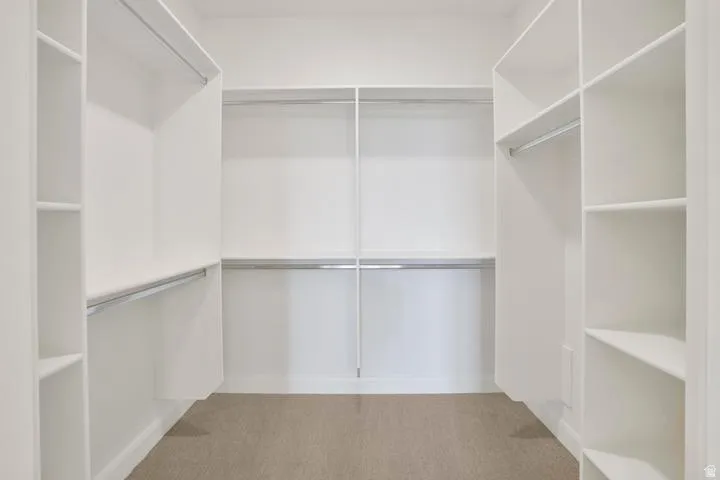 Walk-in closet featuring white built-in shelving, multiple hanging rods, and carpeting