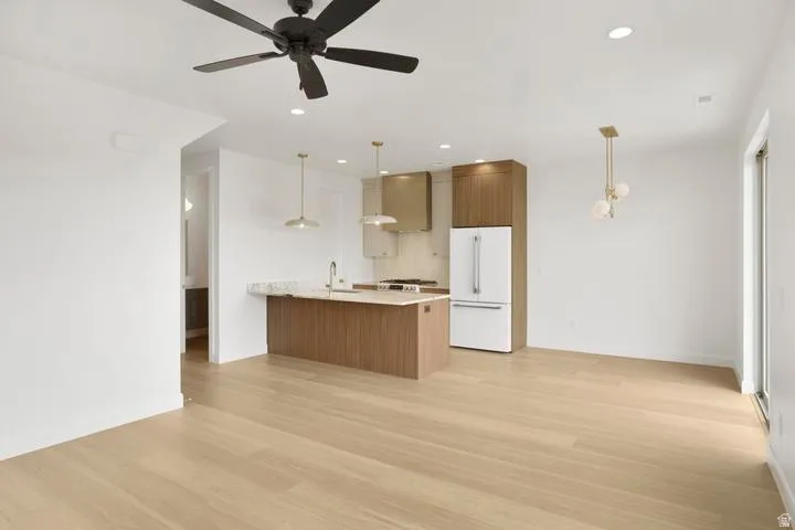 Modern kitchen featuring an island with a light-toned countertop, stainless steel appliances, contemporary pendant lighting, and warm wood-finish flooring