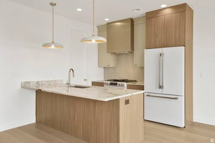Modern kitchen featuring a central island with a sink, light-toned wood-finish cabinetry, and light-colored countertops