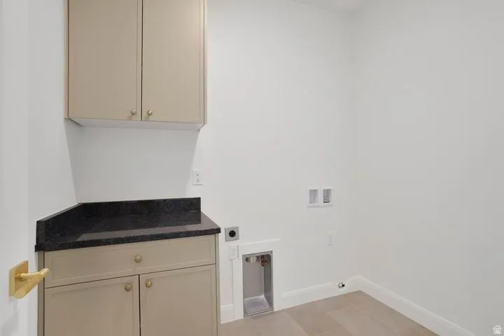 Laundry room featuring light-colored cabinetry with gold-toned hardware, a dark countertop, and tiled flooring
