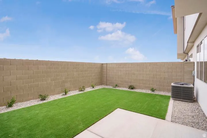 Rear yard featuring a green turf area, concrete patio, gravel borders, and a block perimeter wall