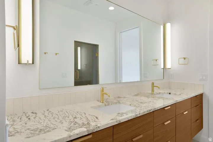 Dual vanity with gold-finish fixtures, a large continuous mirror, and under-mount sinks