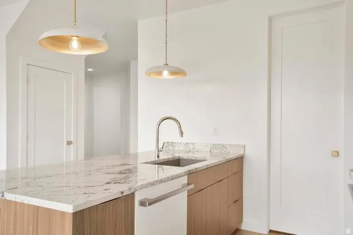 Kitchen island featuring a stone countertop, an undermount sink with a gooseneck faucet, and integrated dishwasher