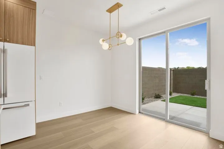 Open concept space featuring light wood-finish flooring, a contemporary gold-tone chandelier, and a built-in refrigerator with wood-paneled cabinetry