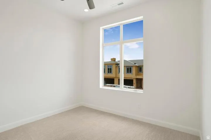 Bright room featuring a large multi-pane window, neutral-toned carpeting, white baseboards, and recessed ceiling lighting