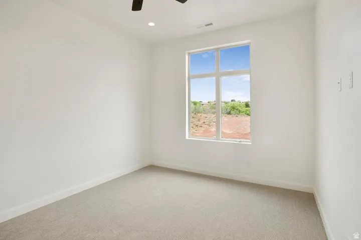 Light-filled room featuring a large window, neutral carpeting, white baseboards, and a ceiling fan with integrated lighting