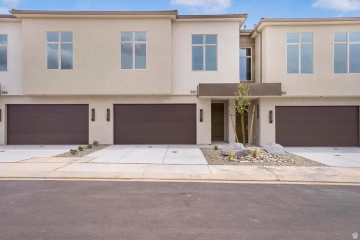 Modern townhome exterior featuring contemporary architecture, light-colored stucco facade, large multi-pane windows, and integrated two-car garage