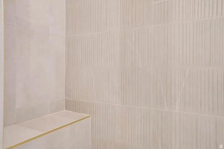 Shower enclosure featuring a built-in bench, smooth light-toned tile, and textured vertical-groove accent tile