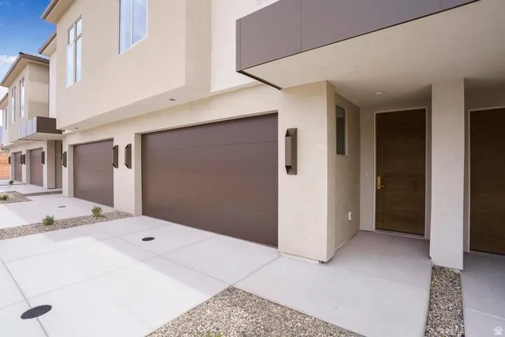 Modern exterior with a brown wood-finish front door, flat panel garage doors, and stucco siding