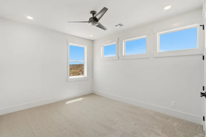 Bright interior space featuring multiple windows, a ceiling fan with integrated lighting, recessed overhead lighting, and neutral carpet flooring