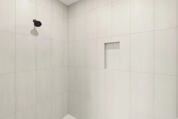 Shower enclosure with large format white tile walls, a matte black shower head, a recessed niche, and a white hexagonal tile floor
