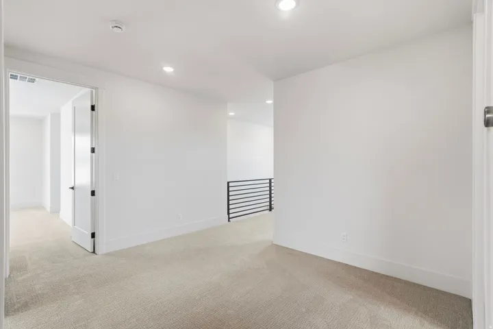 Carpeted hallway with white walls and recessed lighting
