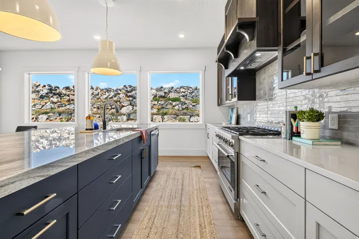 Gourmet kitchen featuring a large island with an undermount sink, dark cabinetry, light countertops, a built-in range, and a tiled backsplash