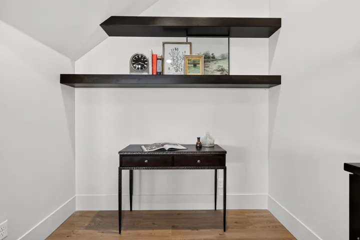 Attic space featuring two dark wood-finish floating shelves, crisp white walls, and wood-finish flooring
