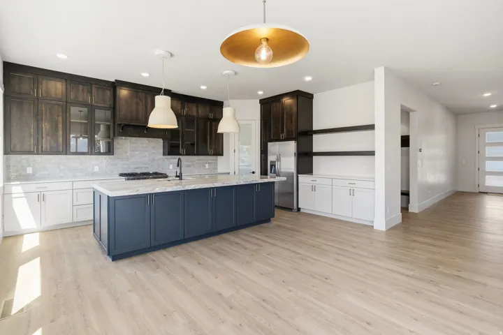 Open-concept kitchen featuring an oversized island with a dark blue base, light wood-finish flooring, stainless steel appliances, dark wood upper cabinetry, and white lower cabinetry