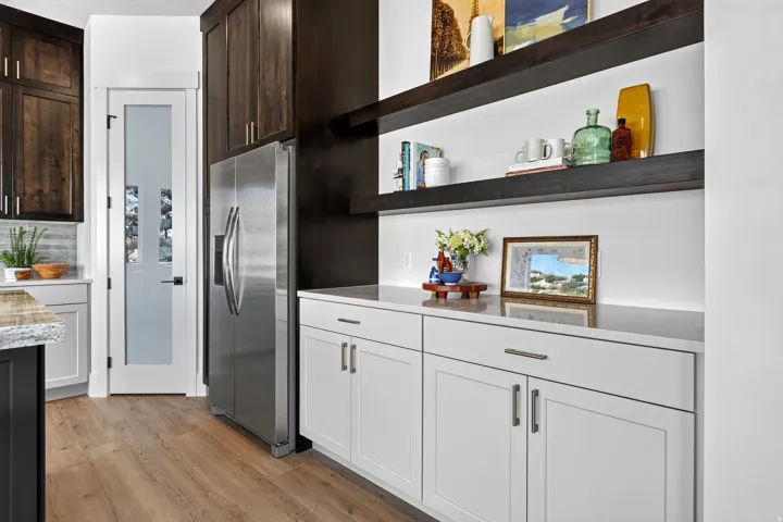 Kitchen featuring stainless steel refrigerator, white shaker-style cabinetry with matte gray hardware, and a stone-finish countertop