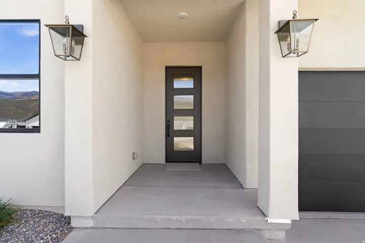 Modern entry featuring a dark-toned door with four rectangular lites, flanked by two bronze-finished lantern sconces