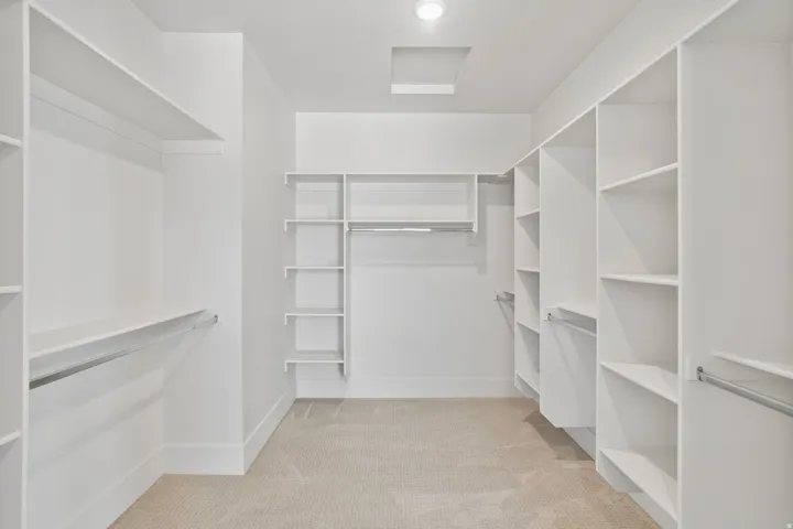 Spacious walk-in closet featuring extensive built-in shelving, multiple hanging rods, recessed ceiling lighting, and light-toned carpeting