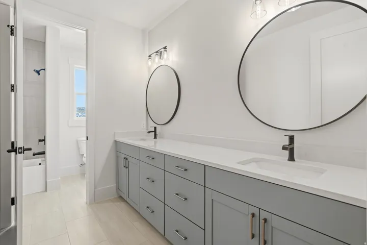 Dual vanity with light gray cabinetry, integrated sinks, white countertops, and circular black-framed mirrors