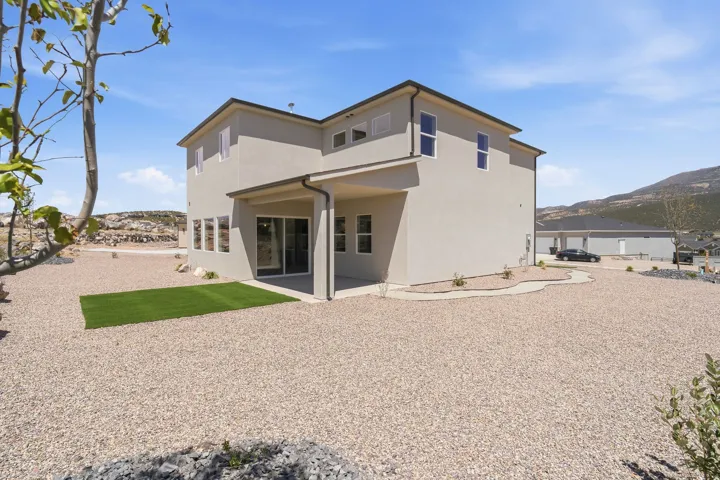 Contemporary stucco exterior with a covered patio, artificial turf accent, and sliding glass door