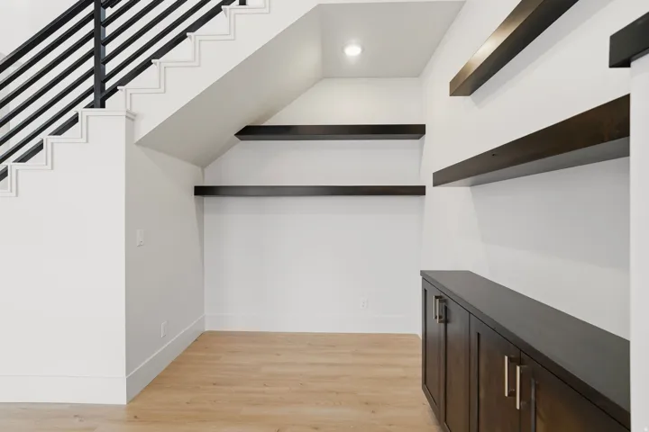 Staircase with contemporary black metal railings, light wood-finish flooring, recessed lighting, built-in shelving, and dark wood cabinetry with brushed nickel hardware
